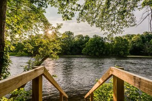 A wooden deck overlooking a calm river with lush greenery and trees in the background. - Peaceful Riverfront Gem + SNP Mountain Magic w/ Hot Tub & 6-8 Person Sauna (Shenandoah)