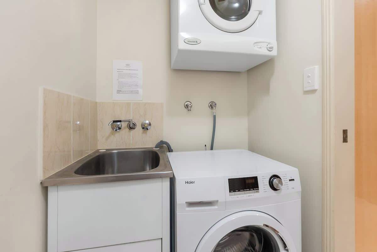A compact laundry area with a washing machine, a sink, and a wall-mounted dryer.