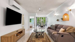 Uma sala de estar moderna com uma TV de tela plana, um armário de madeira, um sofá, um tapete estampado e um ventilador de teto.