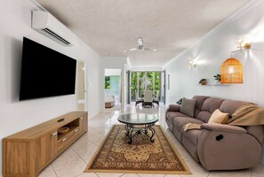 Una sala de estar moderna con un televisor de pantalla plana, un mueble de madera, un sofá, una alfombra estampada y un ventilador de techo.