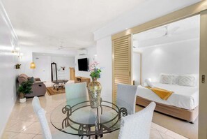 Une chambre d’hôtel moderne avec un lit, une table ronde en verre entourée de chaises, un téléviseur et un canapé.