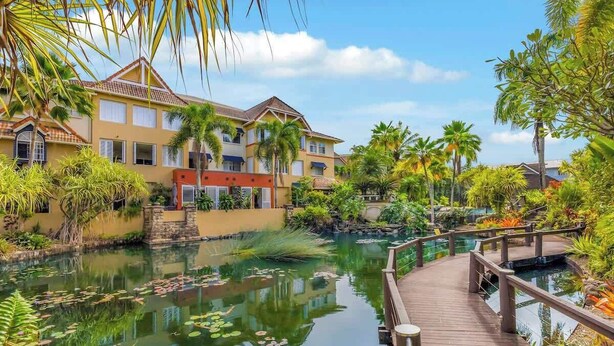 Um resort com área de água, deck de madeira e vegetação tropical.