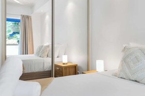 Una habitación de hotel con cama, mesitas de noche, un espejo y vistas al exterior.
