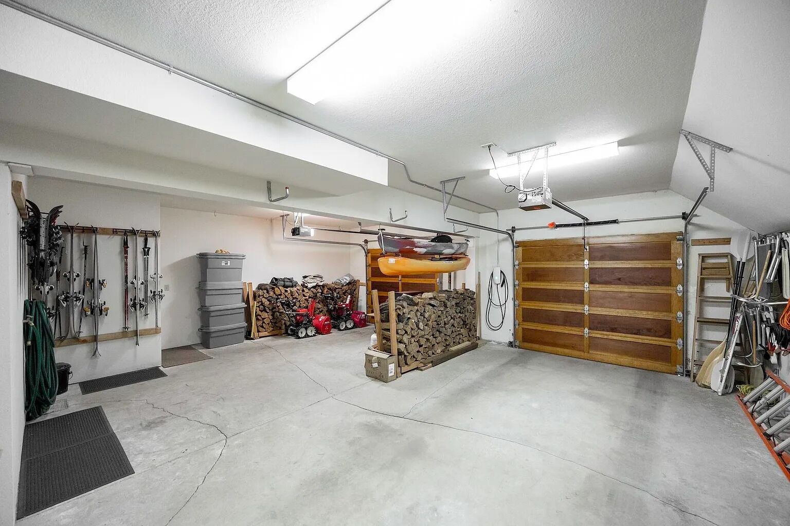 Un garage doté d’un sol en béton, d’une porte de garage en bois, ainsi que de divers outils et équipements.