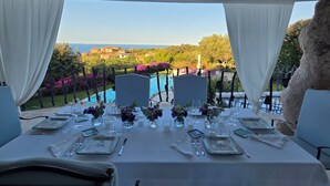 An outdoor dining area with a table set for two, overlooking a pool and a scenic view of houses and greenery. - Villa with pool Porto Cervo (Pantogia)