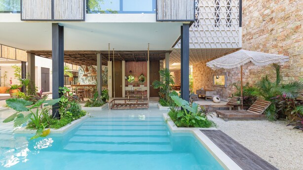 Un edificio moderno con piscina, mobiliario exterior y abundante vegetación.