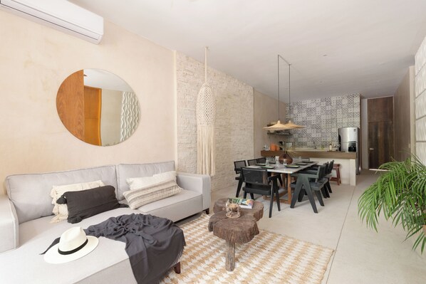Una sala de estar moderna con sofá, mesa de comedor y sillas. Cuenta con una zona de cocina con estufa y lavaplatos.
