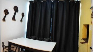 Ein Essbereich mit einem weißen Tisch, schwarzen Stühlen, einem schwarzen Vorhang und einer gelben Wand mit einem kleinen Fenster.