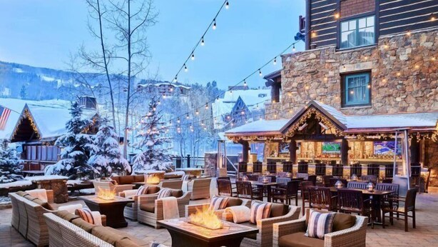 An outdoor seating area with wicker furniture and fire pits, a bar with a stone facade, and snow-covered trees. - Bachelor Gulch Ritz-carlton 2 Bedroom Residential Suite - Ski In, Ski Out (Avon)