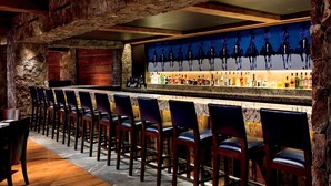 A bar area with stone walls, a long counter with bar stools, and a wall-mounted liquor display. - Bachelor Gulch Ritz-carlton 2 Bedroom Residential Suite - Ski In, Ski Out (Avon)