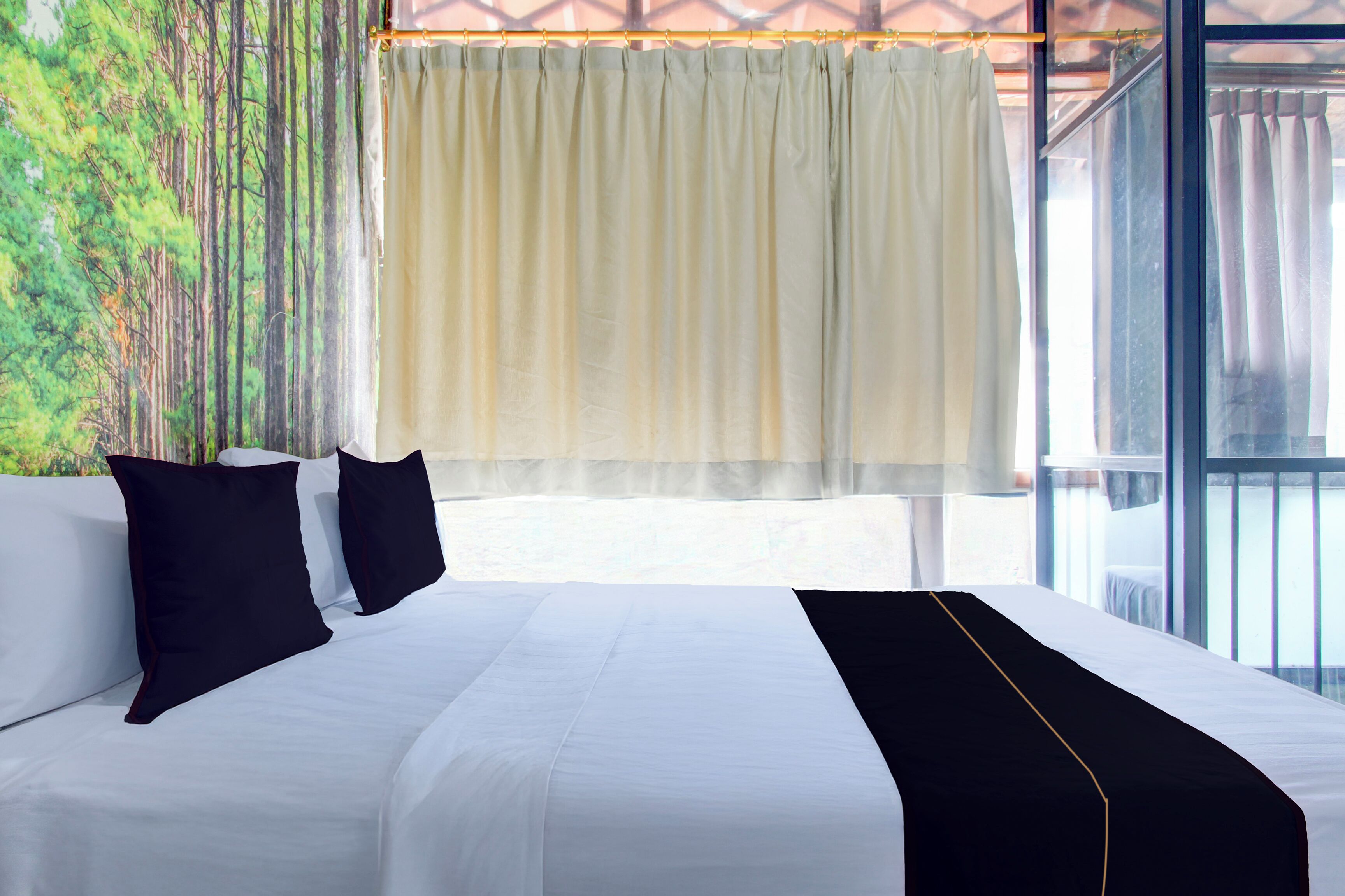A hotel room with a large bed, white bedding, black pillows, a black throw, and a view of trees through the window.
