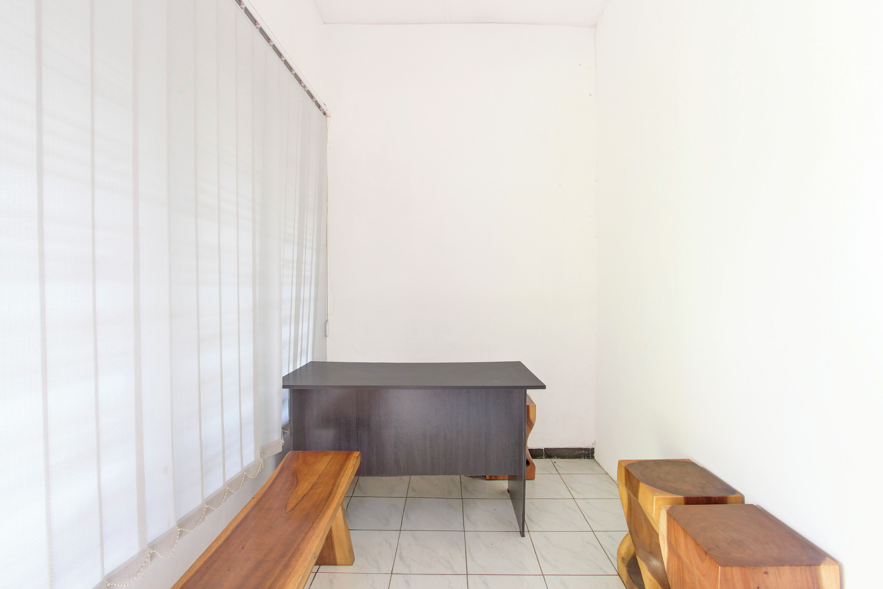 A room with a dark wooden desk, two wooden benches, and a white tiled floor.