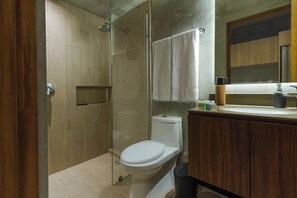 A modern bathroom with a glass shower enclosure, a toilet, a sink with toiletries, and a mirror. - Tuk Viento PH with Private Pool (Tulum)