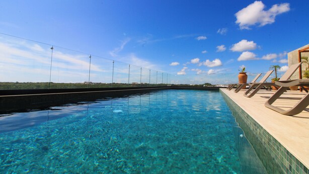 A clear blue pool with a tiled edge, surrounded by lounge chairs and potted plants, under a clear sky. - Tuk Viento PH with Private Pool (Tulum)