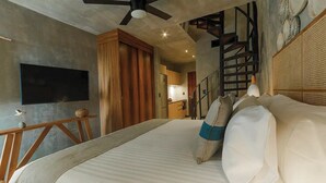 A bedroom with a large bed, a ceiling fan, a flat-screen TV, wooden cabinets, and a staircase leading to an upper level. - Tuk Viento PH with Private Pool (Tulum)