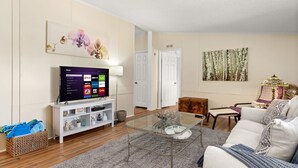 A living room with a flat-screen TV, a glass coffee table, a sofa, and a painting on the wall. - Firefly Lakehouse: 3 br, 2 ba, pet friendly (Canyon Lake)