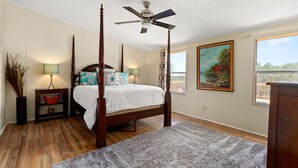 A four-poster bed with a ceiling fan, a painting, and a window with a view. - Firefly Lakehouse: 3 br, 2 ba, pet friendly (Canyon Lake)