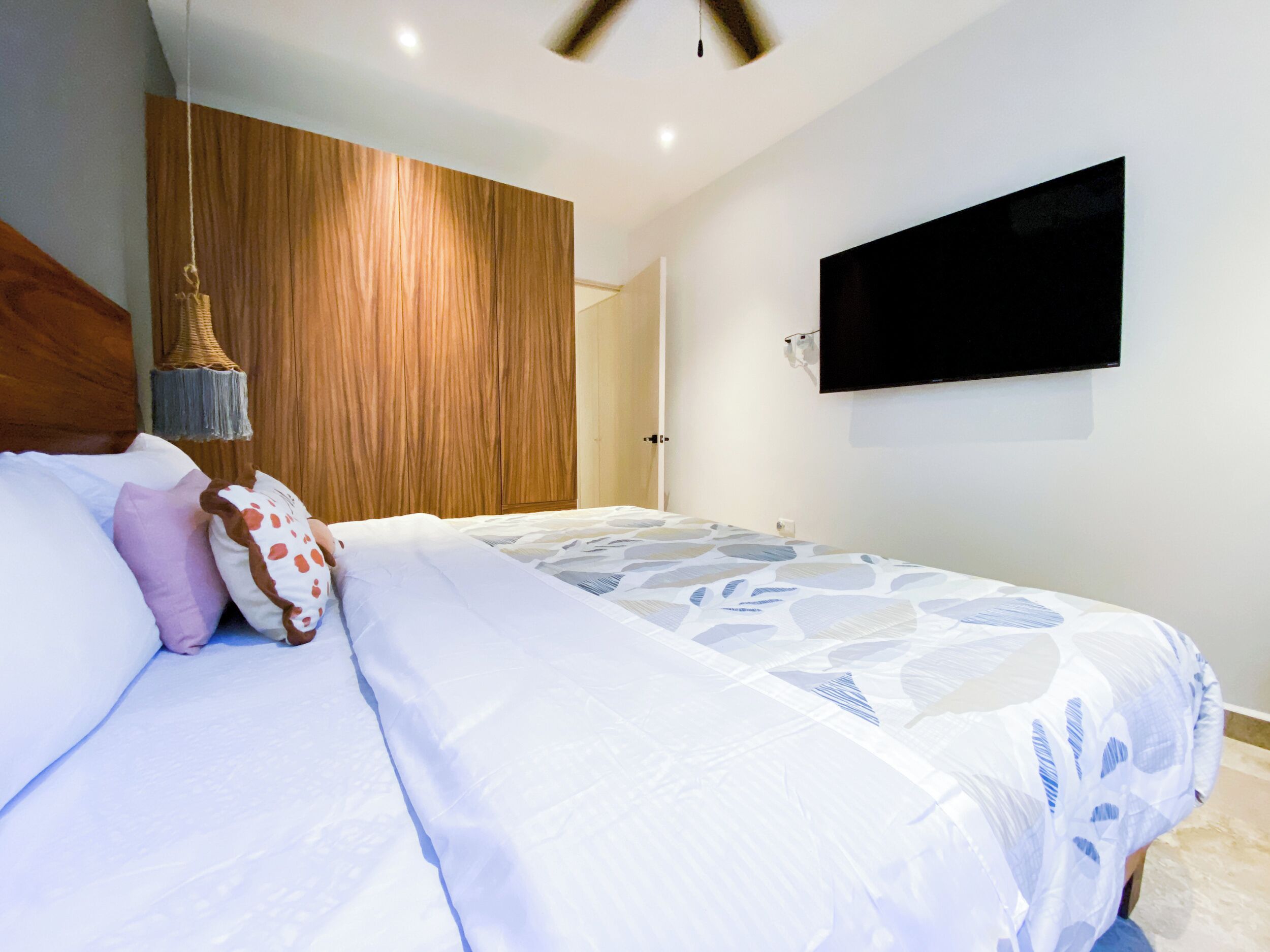 Una camera da letto moderna con un letto grande, un armadio in legno, una televisione a parete e una ventola a soffitto.