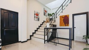 Eine Treppe mit schwarzer Geländer, ein kleiner Tisch mit einem Stuhl und eine Tür links.
