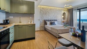 A modern hotel room with a kitchen, a bed with a view, and a dining area with a table and chairs.