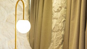 A bathroom with a stone wall, a wooden vanity, a round mirror, a gold floor lamp, and a white stool.