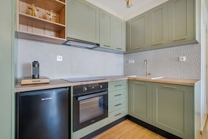 A kitchen with green cabinets, a black dishwasher, a built-in oven, and a wooden countertop.