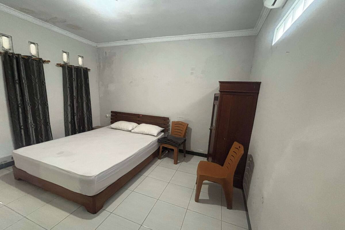 Ein Schlafzimmer mit einem Einzelbett, zwei Stühlen, einem Kleiderschrank und einem Fenster.