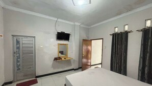 A bedroom with a bed, a television mounted on the wall, a mirror, a door, and curtains. - OYO 95050 Penginapan Sekarsari Syariah (Yogyakarta)