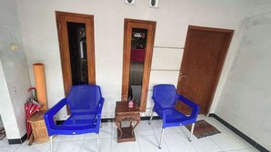 A small room with two blue plastic chairs, a wooden table, and a mirror. There are two doors, one with a red curtain and another with a sign. - OYO 95050 Penginapan Sekarsari Syariah (Yogyakarta)