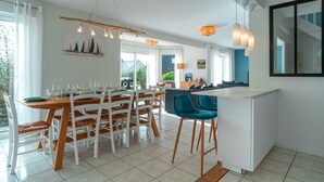 Una cocina moderna con armarios blancos, una isla central y un comedor con sillas blancas y una mesa de madera.