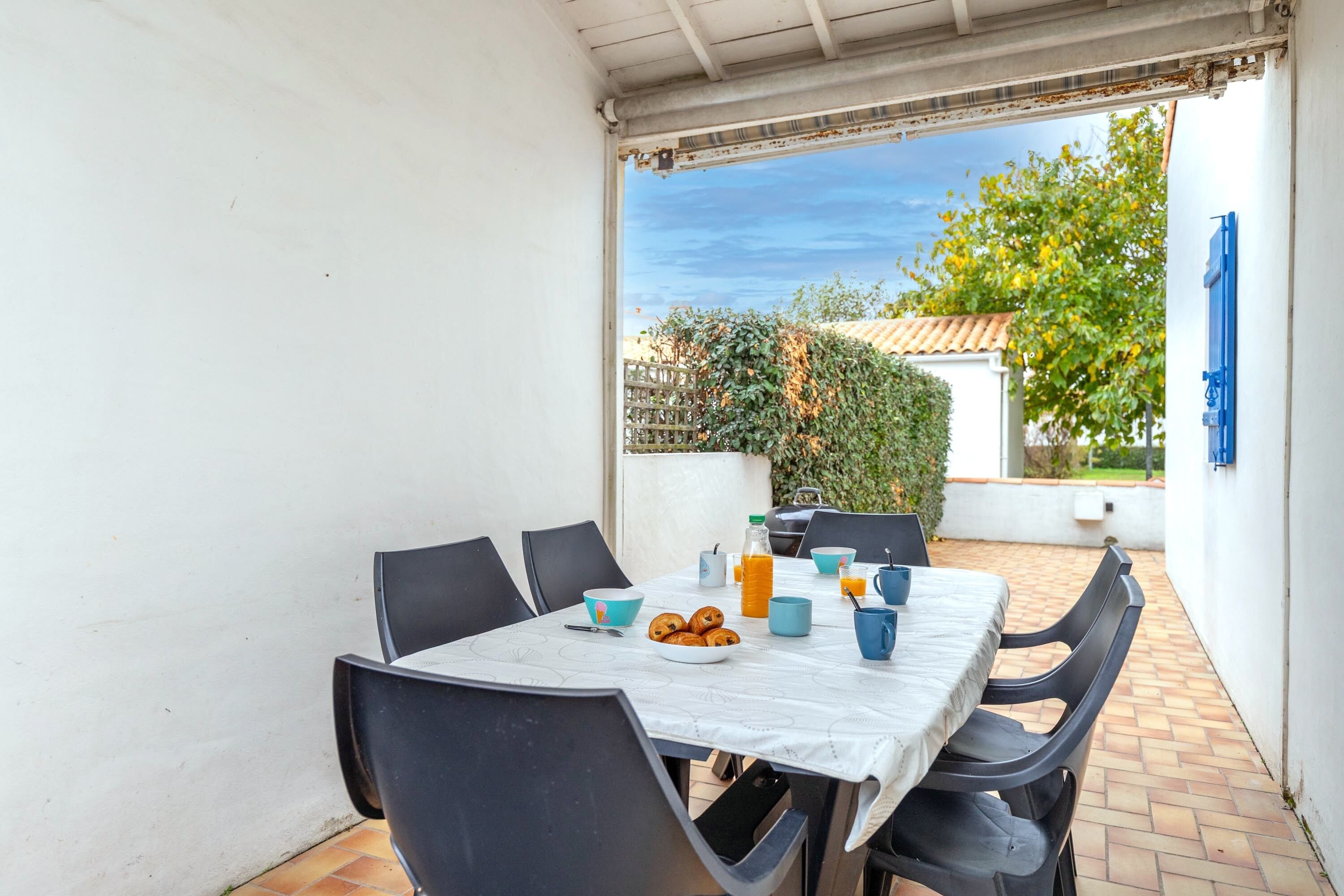 Un patio con una mesa dispuesta para el desayuno, que incluye cruasanes y zumo de naranja, y vistas a un jardín y un edificio al fondo.