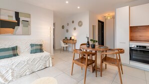 A modern living room with a sofa, wooden chairs, a dining table, and a kitchen area with an oven. - A Terrazzo di Calypso - Grande Terrasse (Grosseto-Prugna)