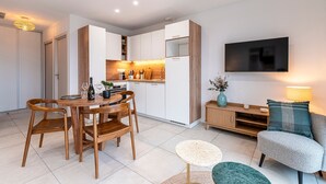 A modern kitchen with white cabinets, a dining table with wooden chairs, a TV mounted on the wall, and a cozy seating area with a sofa and a lamp. - A Terrazzo di Calypso - Grande Terrasse (Grosseto-Prugna)