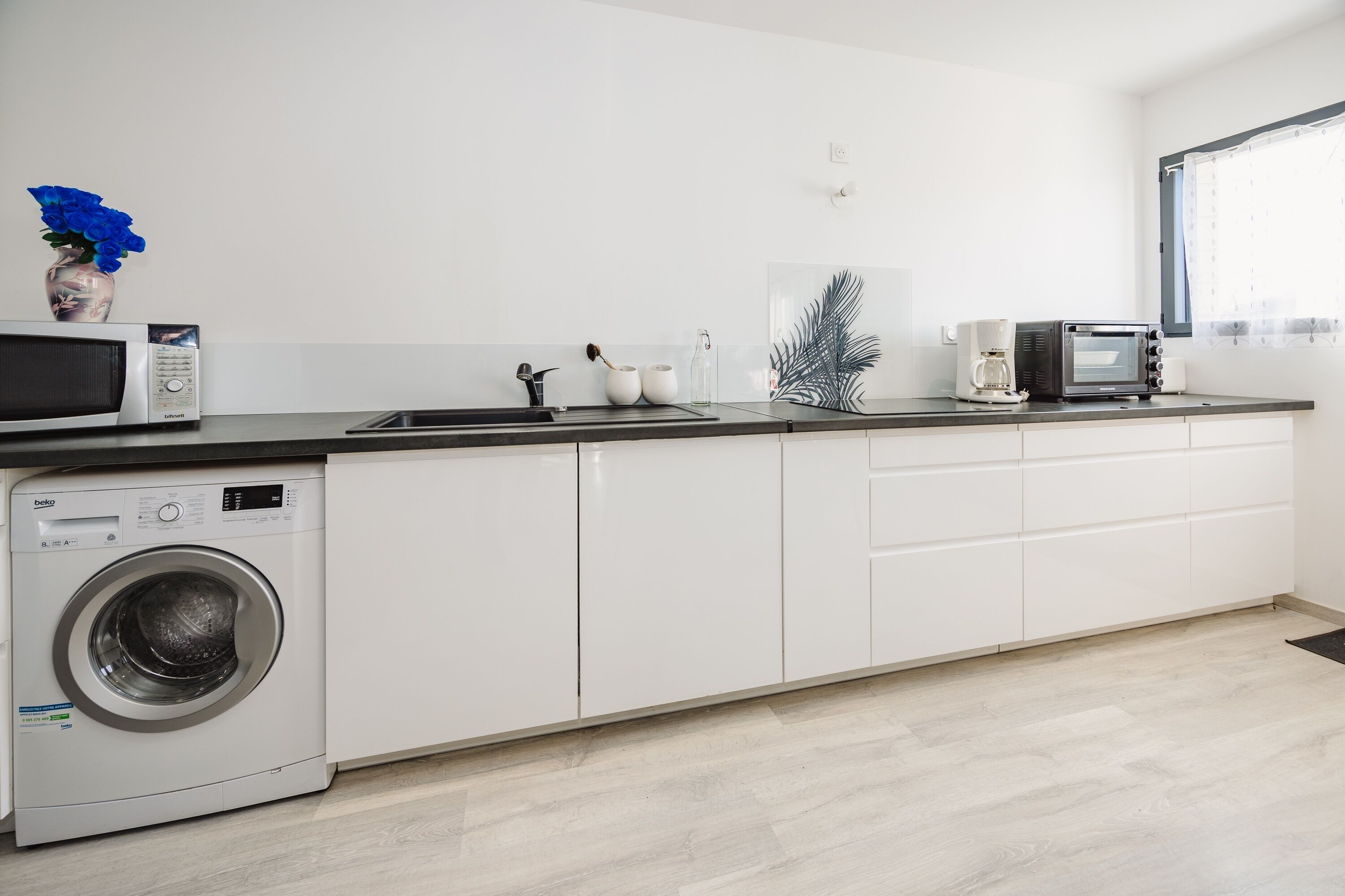 Une cuisine moderne équipée d’un lave-linge, d’un four à micro-ondes et d’une machine à café.