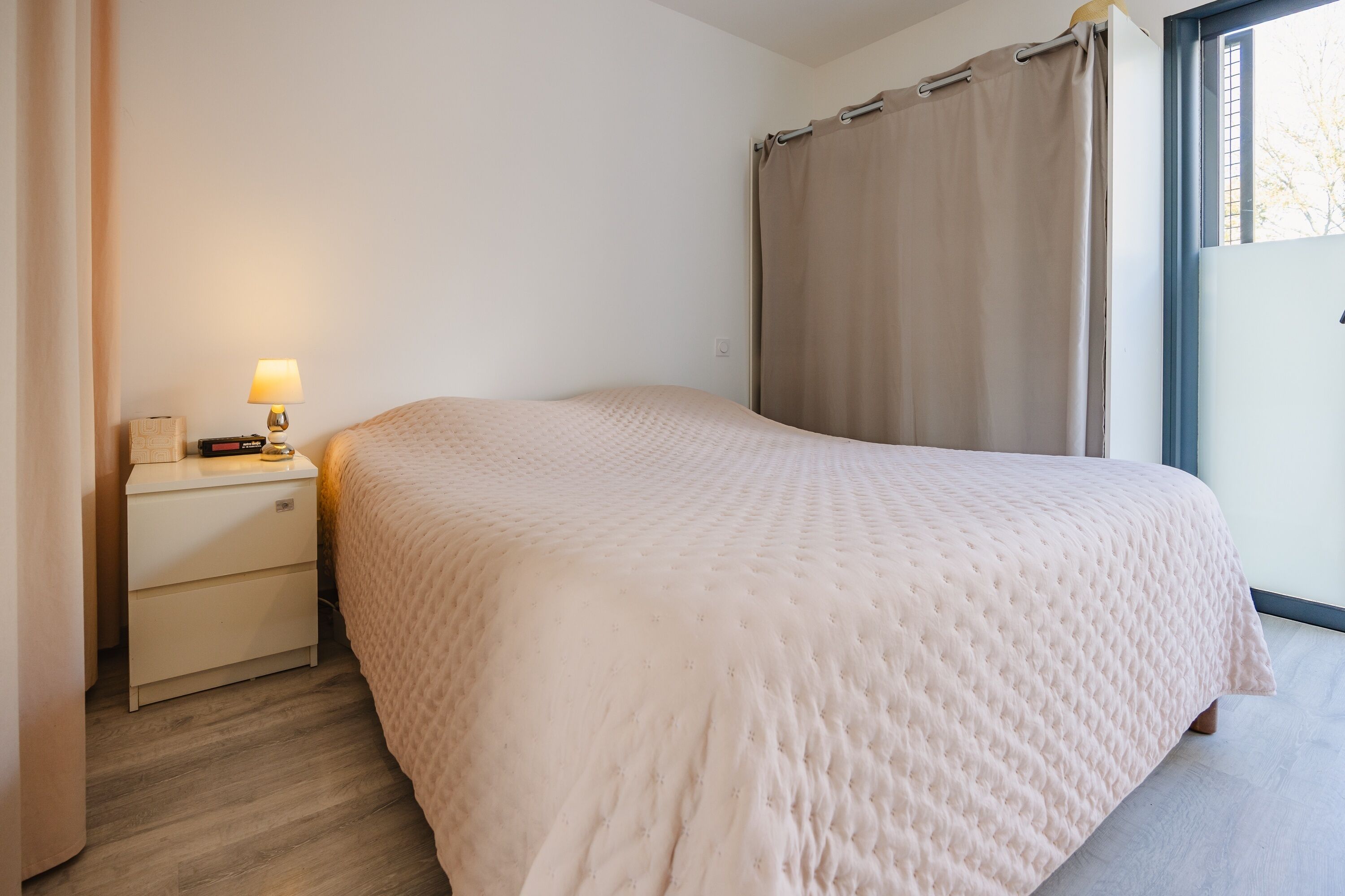 A bedroom with a bed, a nightstand, a lamp, and a window with curtains.