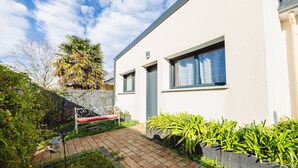 Une maison moderne avec une façade blanche, un chemin en briques et un petit jardin agrémenté de plantes et d’un banc.
