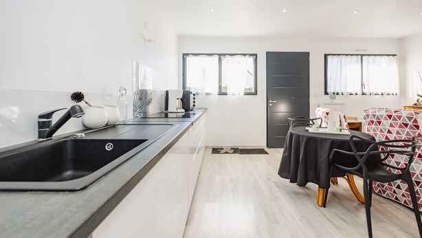 Une cuisine moderne avec un plan de travail noir, un évier et un coin repas comprenant une table et des chaises.
