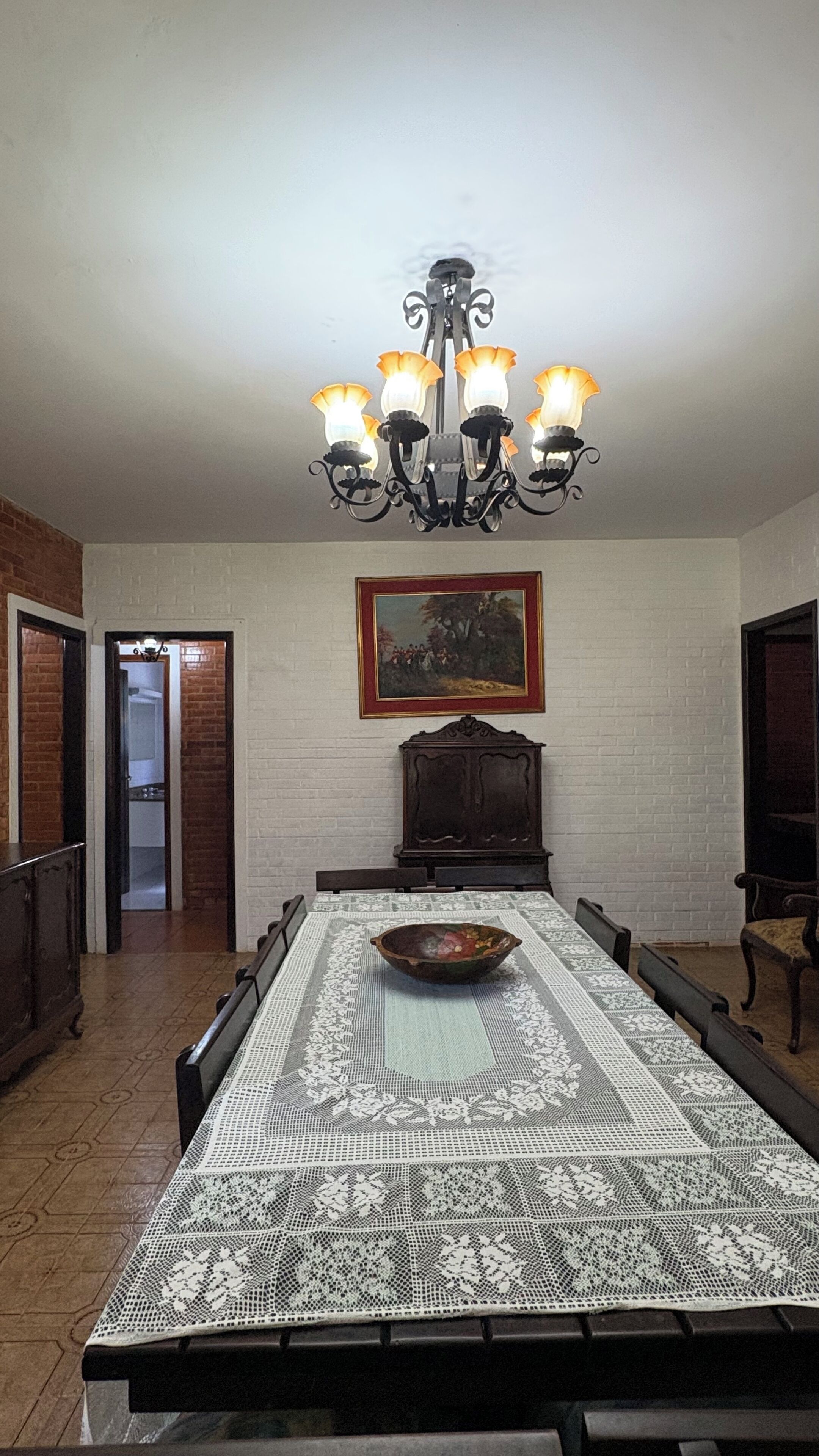Une salle à manger avec une longue table, un lustre, un tableau encadré et un buffet en bois.