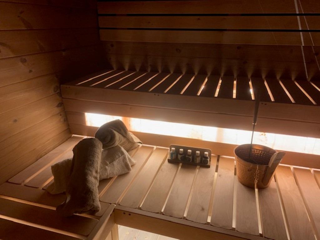 Una sauna amb seients de fusta, una tovallola, una ampolla d'oli i un recipient metàl·lic.