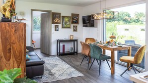 Ein modernes Wohnzimmer mit Essbereich, ausgestattet mit einem Holztisch, bequemen Sitzmöglichkeiten und Bildern an den Wänden.