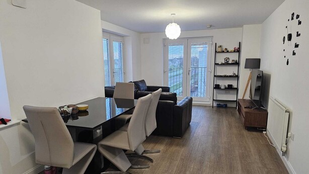 A modern living room with a dining area, featuring a black sofa, a glass dining table, and a large window with blinds. - Stylish 2 Bed Flat Near Airpot with free parking (Edinburgh)