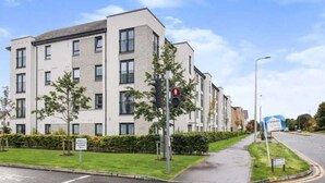 A modern apartment building with a flat facade, multiple windows, and a landscaped front yard with young trees. - Stylish 2 Bed Flat Near Airpot with free parking (Edinburgh)