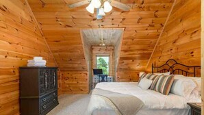 Quarto acolhedor de cabana de madeira, com cama, cômoda e uma mesinha com abajur.