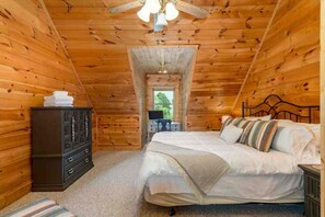 A cozy wooden cabin bedroom with a bed, dresser, and a small table with a lamp. - Lionheart Cabin-Majestic Mountain Escape,Game Room (Maggie Valley)