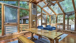 A wooden cabin with large windows, a wooden table, blue sofas, and a ceiling fan. - Sasha’s Hidden Creek Cabin-Magical Views, 12 Acres (Maggie Valley)