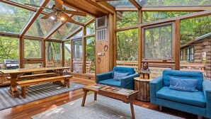 A spacious cabin with a large wooden dining table, blue sofas, and a ceiling fan. - Sasha’s Hidden Creek Cabin-Magical Views, 12 Acres (Maggie Valley)