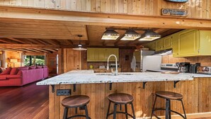 A wooden cabin interior with a kitchen island, bar stools, and a red sofa in the living area. - Sasha’s Hidden Creek Cabin-Magical Views, 12 Acres (Maggie Valley)