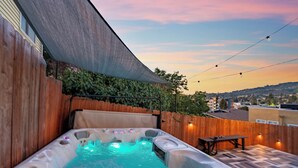Uma banheira de hidromassagem com deck de madeira e vista para o horizonte urbano ao pôr do sol.