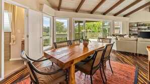 A dining area with a wooden table and chairs, a chandelier, and a view of the outdoors through large windows.