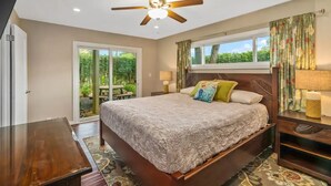 A bedroom with a bed, a ceiling fan, a window with curtains, a nightstand, and a lamp.